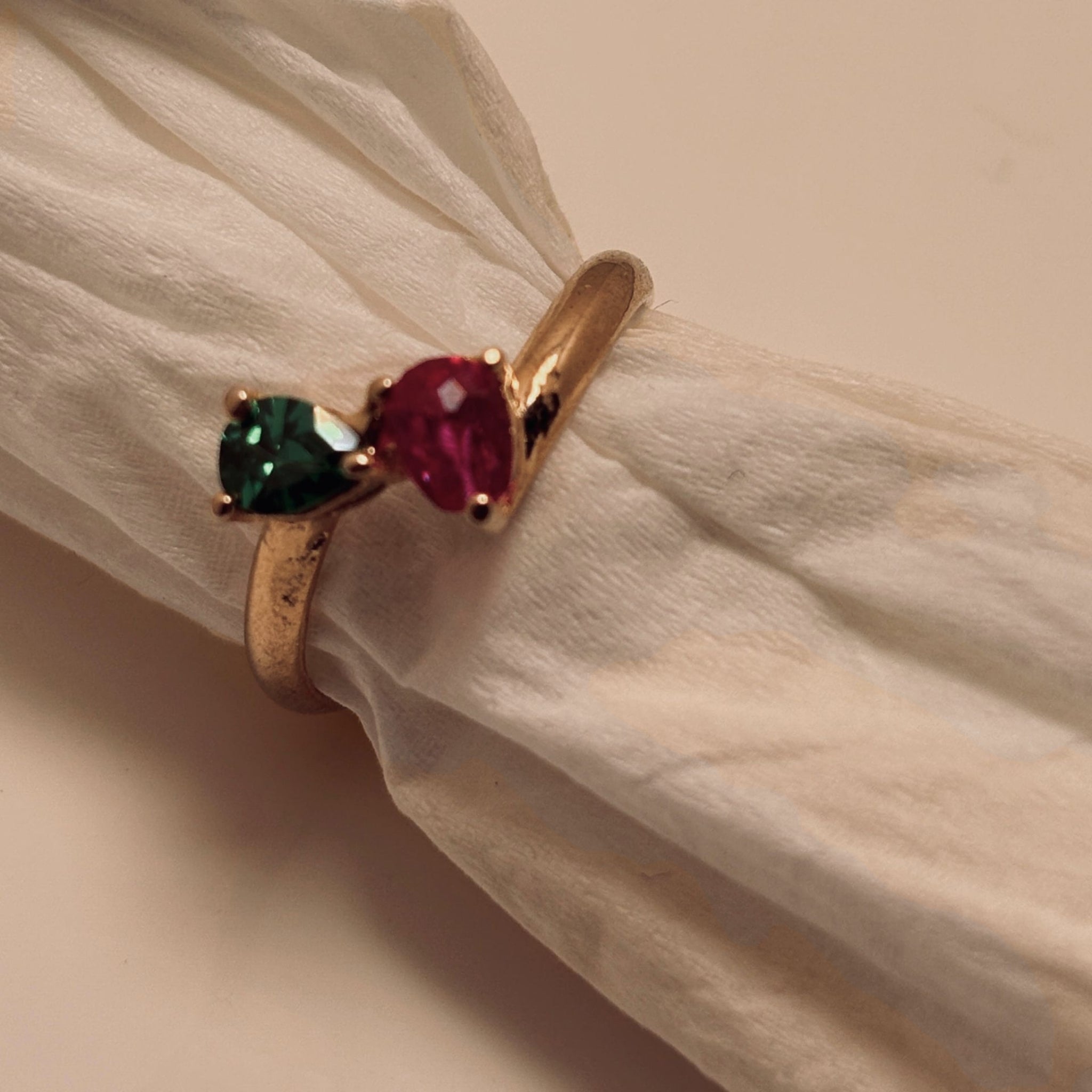 Gold ring with green and red gemstones on a beige fabric background