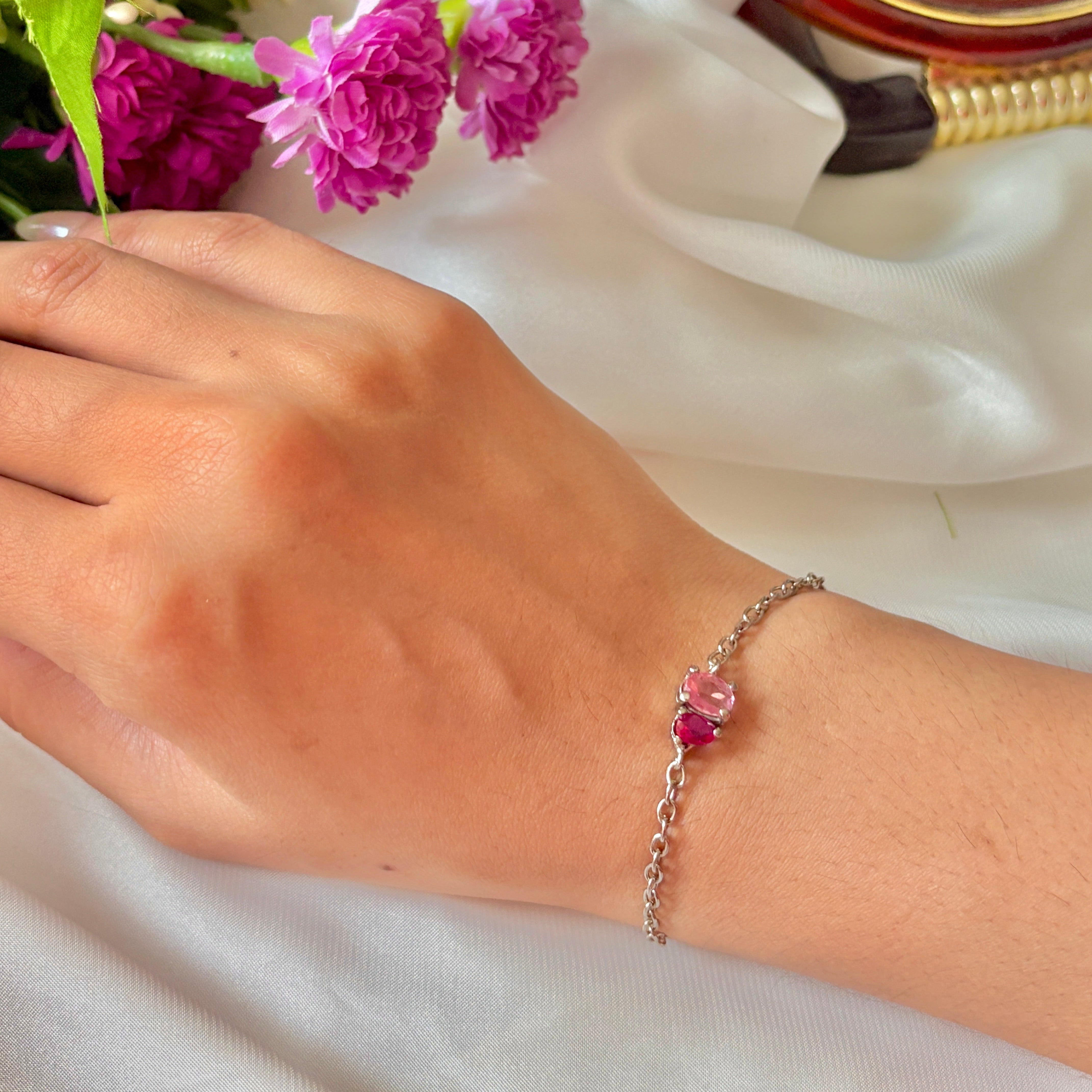 Hand wearing a bracelet with pink flowers, next to a small round mirror and pink flowers.