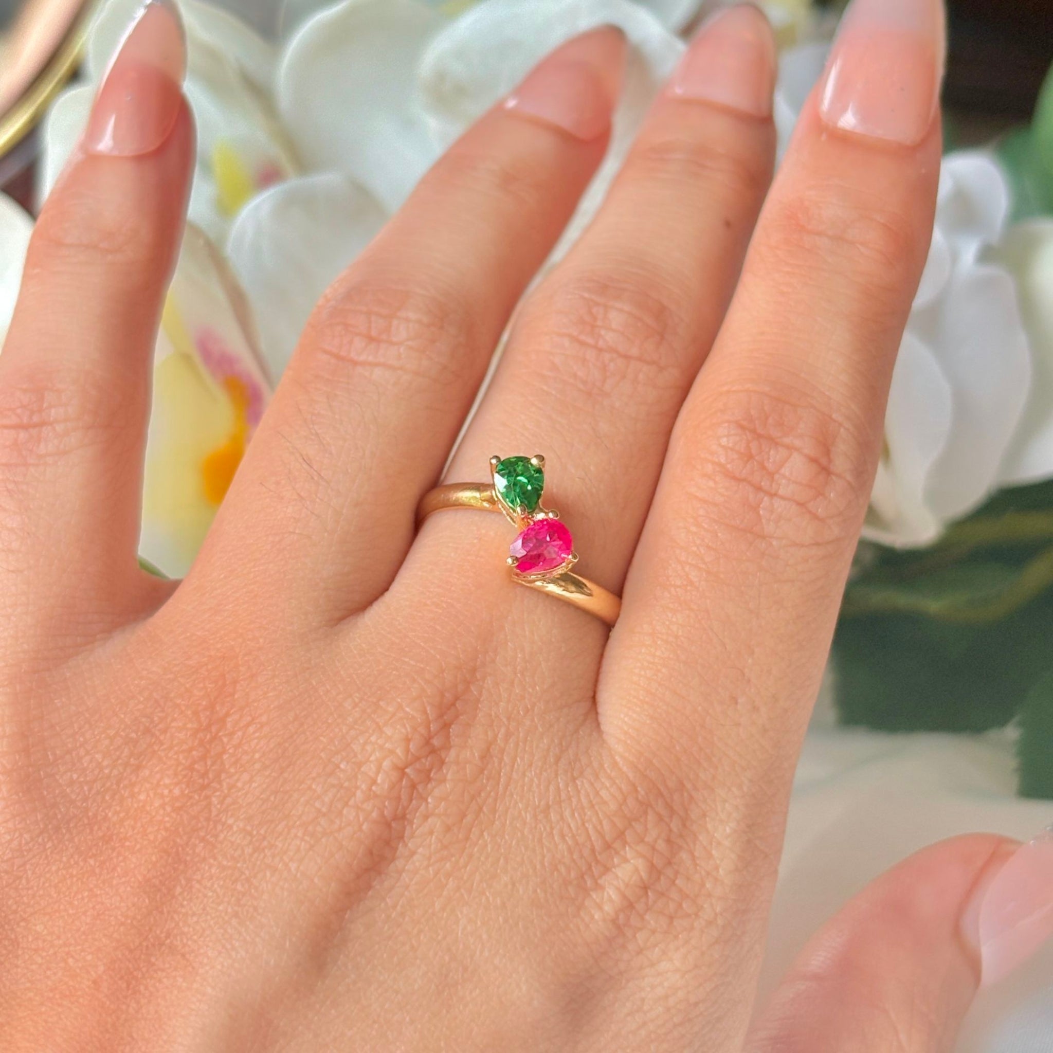 Gold ring with colorful gemstones on a hand against a floral background