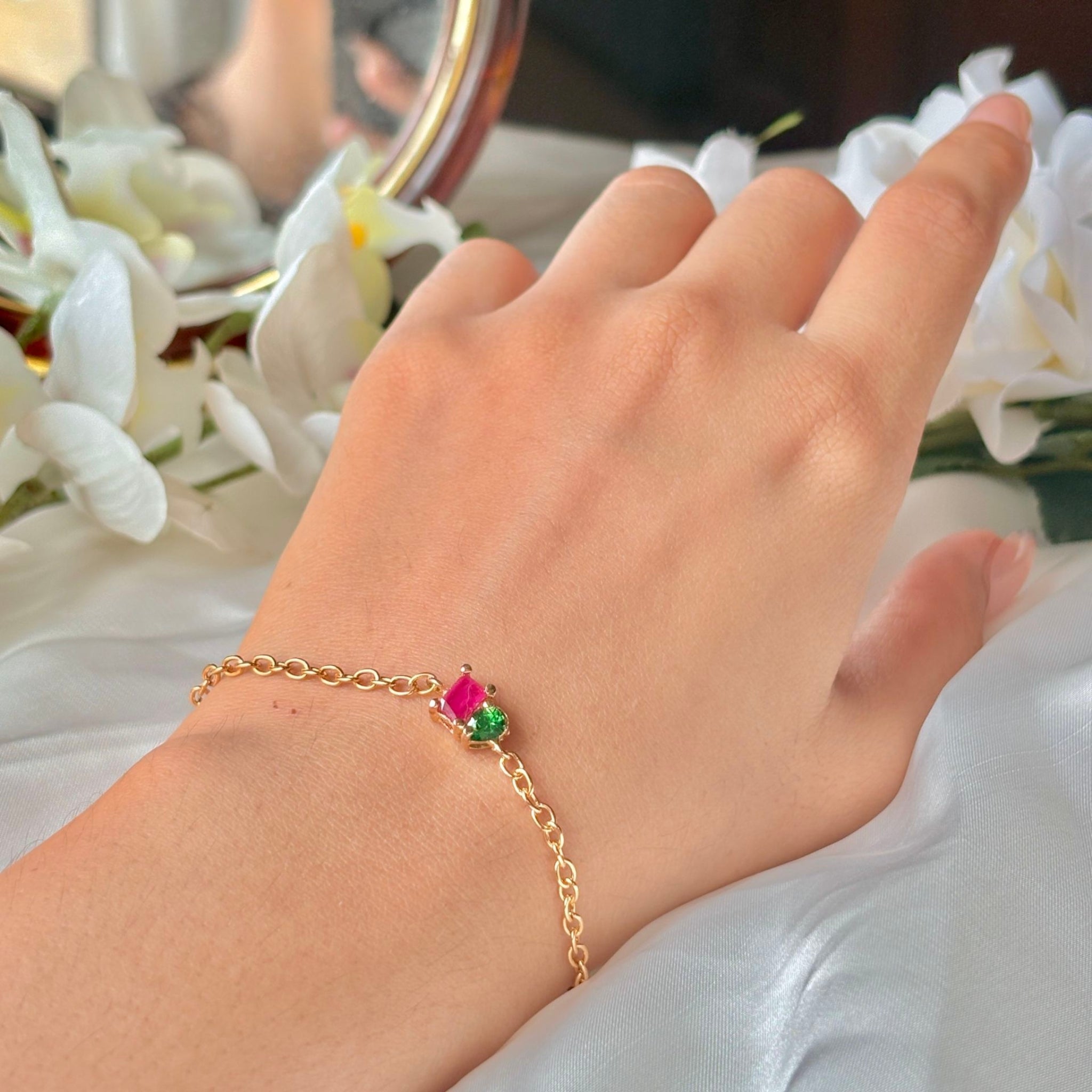 Hand wearing a gold bracelet with colorful charms against a floral background
