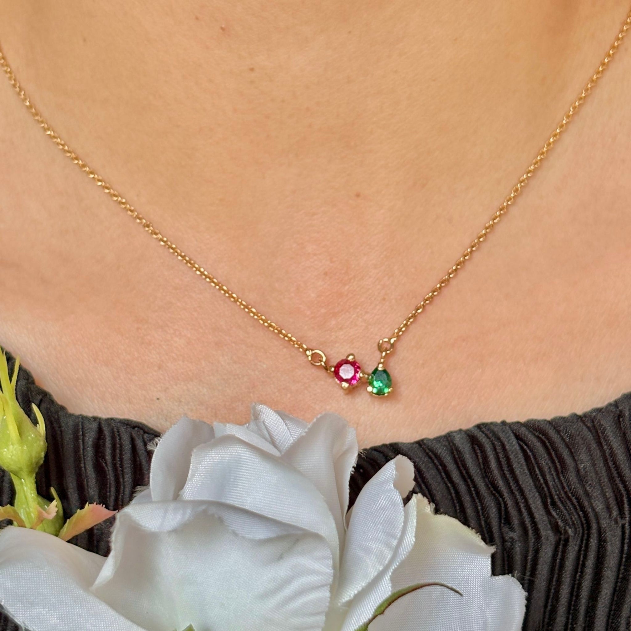 Gold necklace with gemstones worn by a person, with white flowers in the foreground.